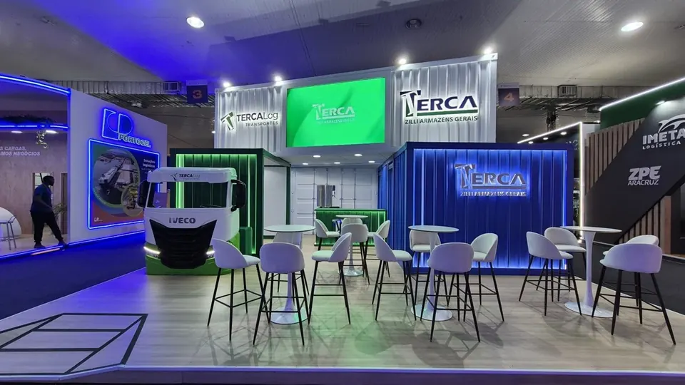 Estande da Zilli Armazéns visto de frente, com área de mesas altas e painel de LED verde.